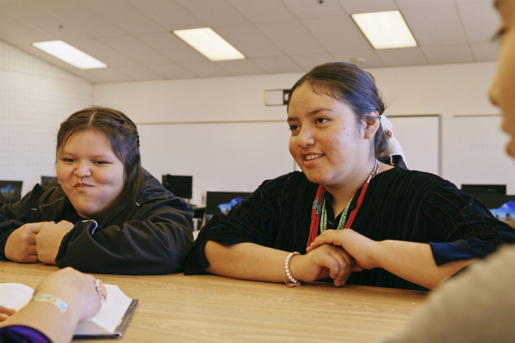 An Indigenous Navajo high school teacher with a group of students in a school library.
