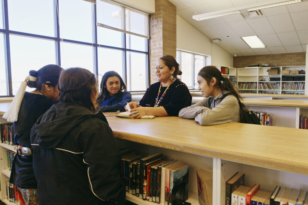 An Indigenous Navajo high school teacher with a group of students in a school library.