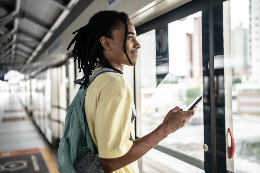 Young man waiting for the train in the subway platform, holding a phone..