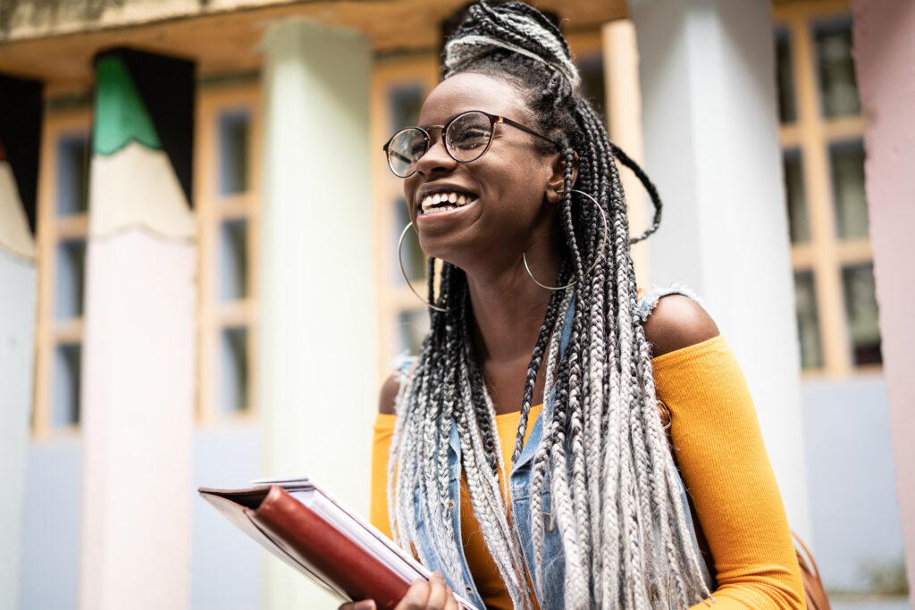 Smiling girl in glasses with braids carrying books.