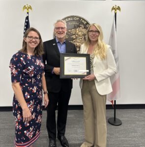 Photo of Cradle-to-Career (C2C) Executive Director, Mary Ann Bates, and  C2C Board Chair Gavin Payne presenting C2C Board Member Debbie Cochrane with a certificate of service at the May 20th C2C Governing Board Meeting.